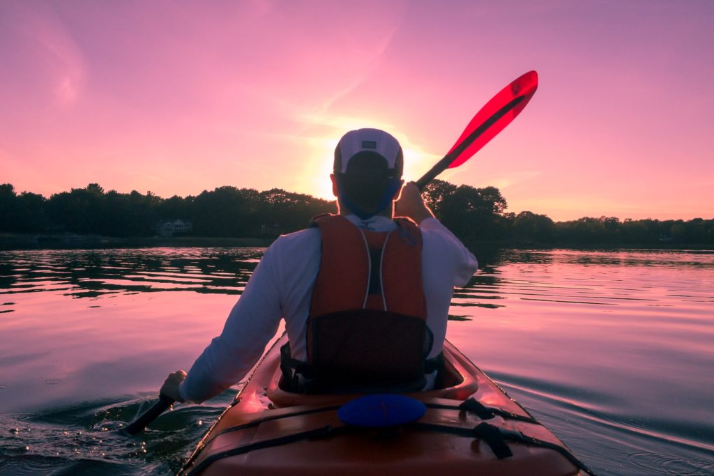 A Kayaking Guide. man kayaking at sunset with red life preserver